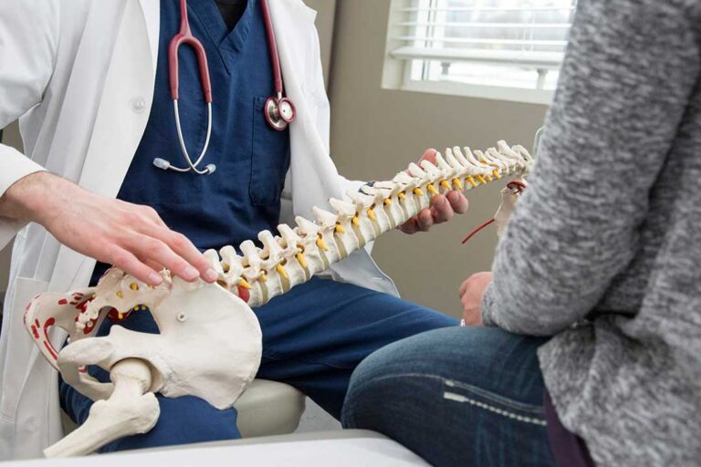 Person applying a wrapped ice pack to the lower back while seated at home.