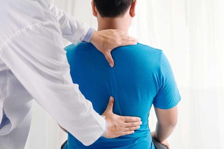 Clinician assessing a seated adult’s spinal posture in a bright examination room