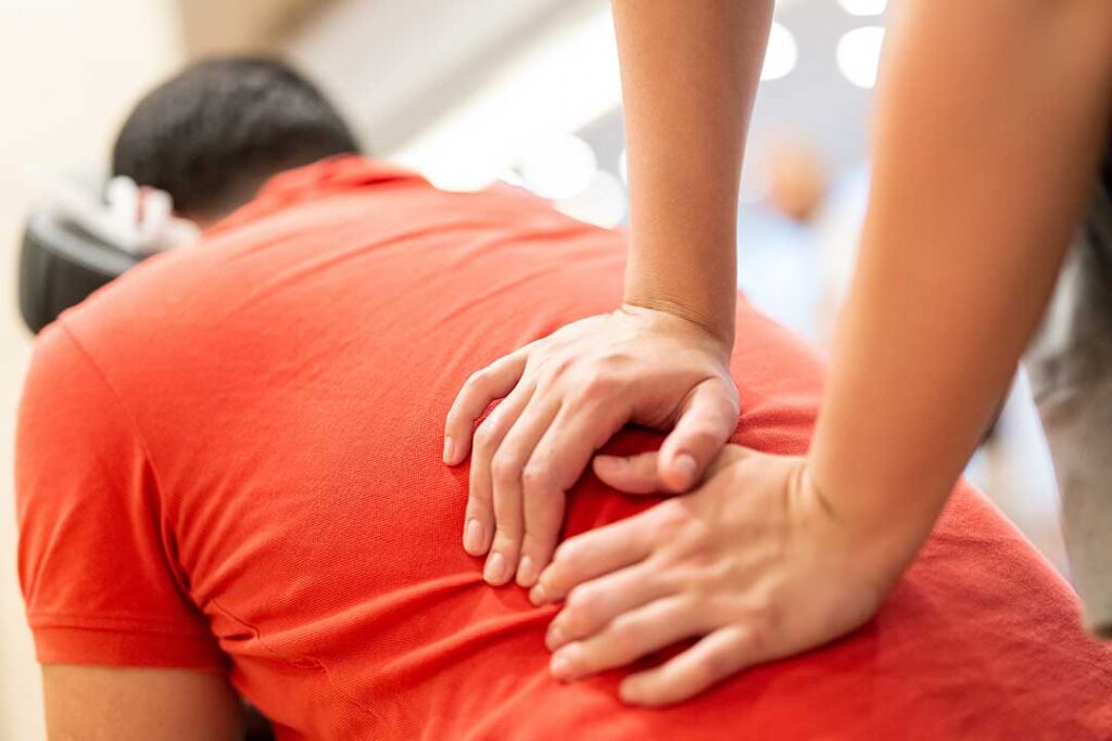 Adult discussing back and neck pain with a clinician during a movement assessment in a bright office.